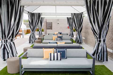 Luxury outdoor lounge area with gray sectional sofas, striped black and white curtains, and brick backdrop