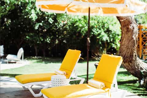 Yellow lounge chairs under umbrella in shaded garden area with trees