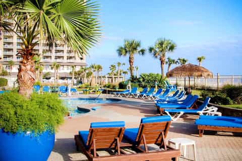 Beachfront resort pool area with blue loungers, palm trees, and oceanview deck