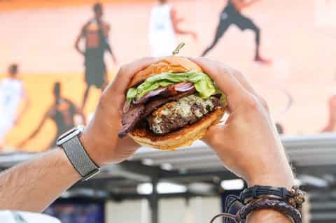 Man holding gourmet burger with lettuce and toppings at beach venue