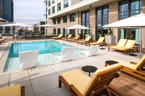 Resort pool deck with loungers, umbrellas, and brick building with yellow cushioned seating