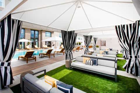 Modern rooftop pool deck with striped cabanas, loungers, and white tent canopies overlooking a building