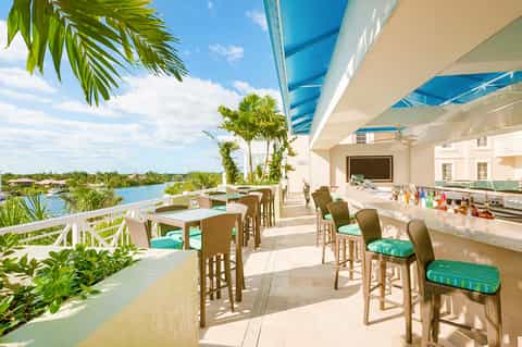 Waterfront bar and patio with wicker seating, turquoise water views, and tropical landscaping
