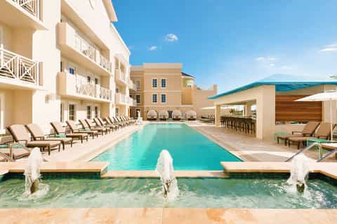 Beachfront resort pool with turquoise water, loungers, and multi-story tan buildings