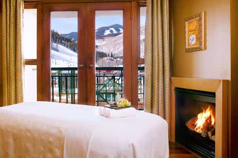 Luxury ski resort bedroom with fireplace, mountain views, and French doors opening to a snowy balcony