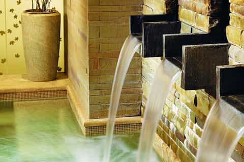 Spa waterfall features cascading water flowing into steaming mineral pool with brick walls