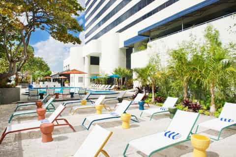 Modern resort pool deck with colorful lounge chairs, stone accents, and tropical landscaping near white building