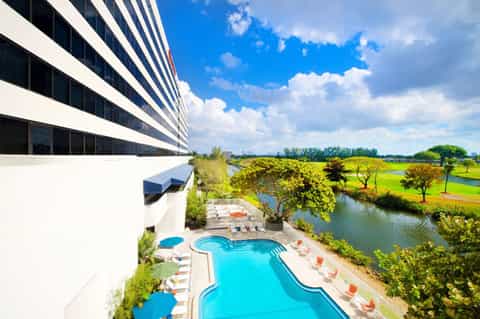 Modern hotel with curved white balconies overlooking a blue pool and surrounding green landscape