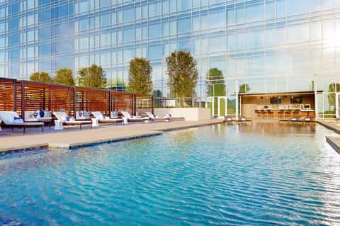 Modern indoor pool with loungers, wooden privacy screens, bar area, and glass building