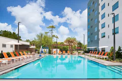 Resort pool with turquoise water, lounge chairs, umbrellas, and modern apartment building