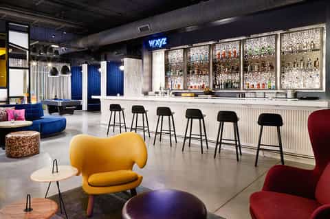 Modern hotel bar interior with blue accent lighting, bar seating, and colorful lounge furniture