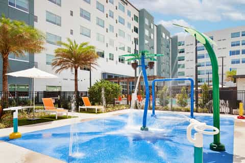 Colorful splash pad with blue water features and palm trees in resort courtyard