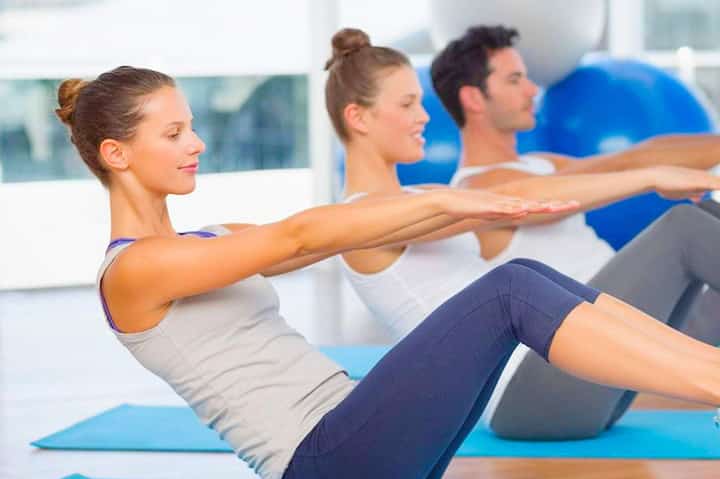 Group fitness class performing pilates exercises on mats in a bright studio with blue stability balls
