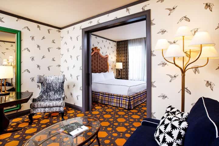 Eclectic hotel room with bird wallpaper, orange patterned carpet, green doorframe, and vintage-inspired furnishings