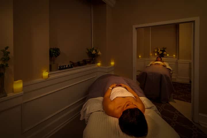 Spa treatment room with person receiving massage on bed under warm candlelit ambiance