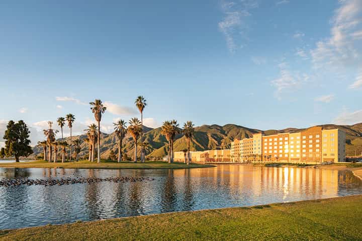 Yellow hotel building reflected in lagoon with palm trees and mountains at sunset