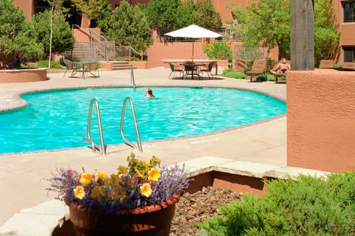 Turquoise resort pool with terracotta buildings, loungers, and desert landscaping in sunny courtyard