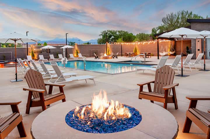 Resort poolside at dusk with fire pit, lounge chairs, umbrellas, and mountain views