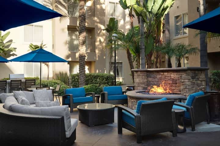 Outdoor courtyard with blue umbrellas, fireplace, tropical plants, and contemporary seating