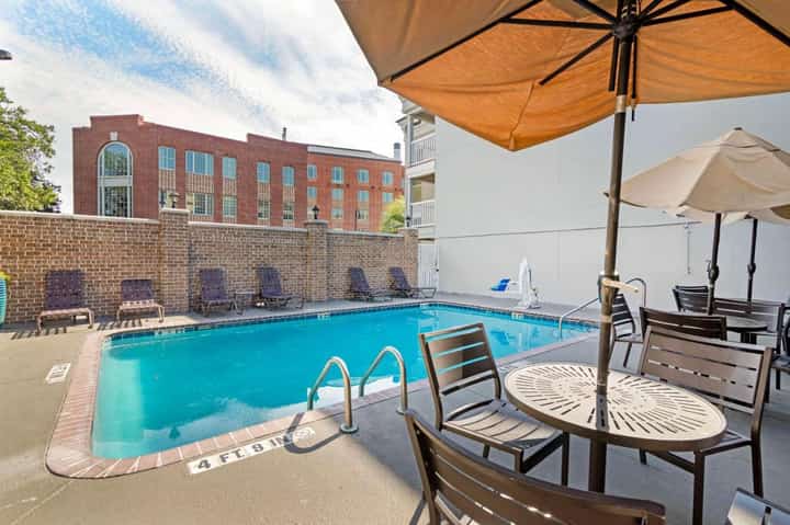 Outdoor swimming pool with blue water, lounge chairs, umbrellas, and brick building backdrop