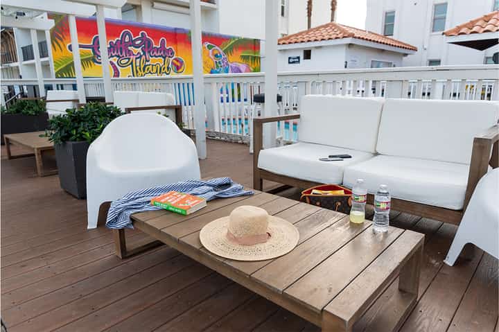 Beachfront deck with colorful mural, white furniture, wooden table with straw hat