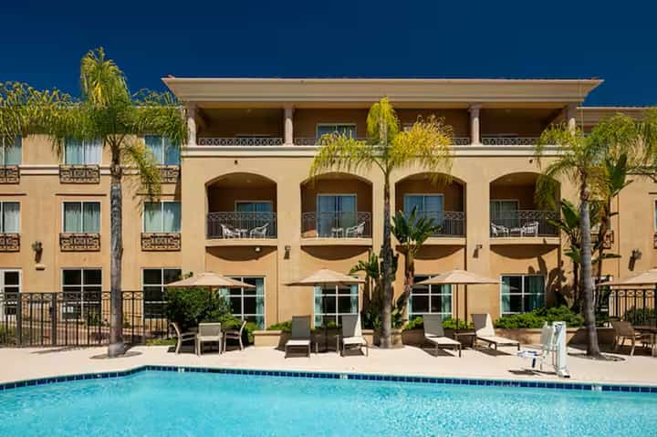 Mediterranean-style resort building with arched windows, palm trees, and resort pool in foreground