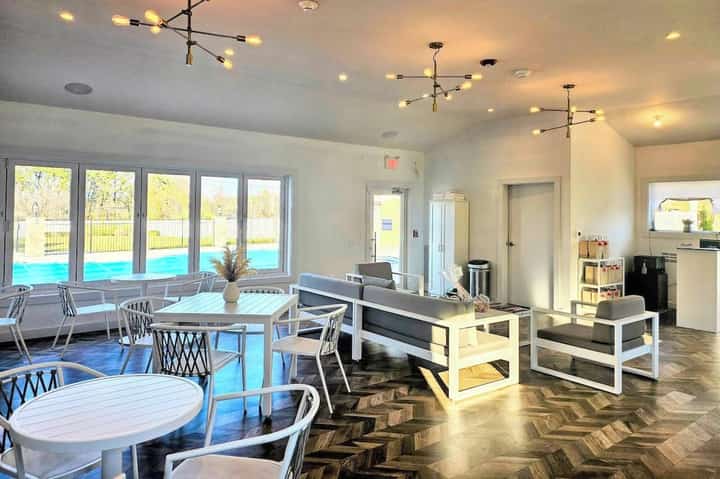 Bright indoor pool lounge with floor-to-ceiling windows, dining area, fireplace, and water views