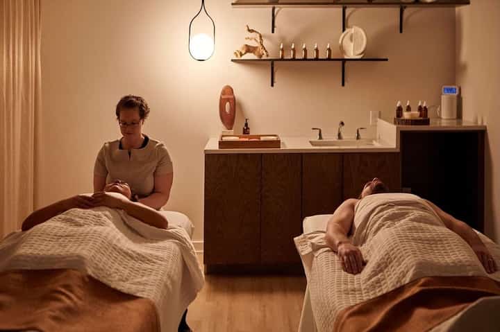 Spa treatment room with two massage tables and therapist preparing wellness service