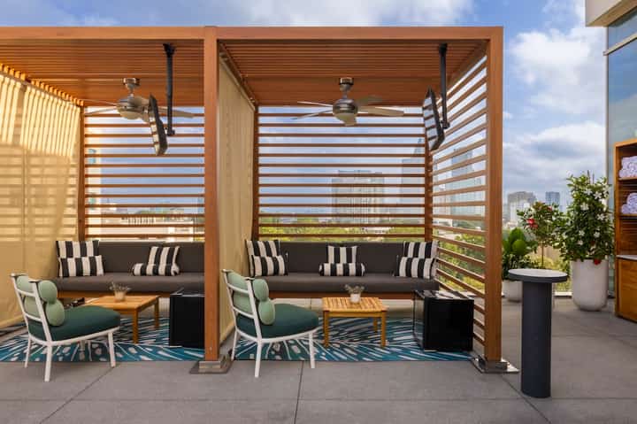 Two wooden pergola cabanas with dark cushioned seating, striped shade panels, and modern patio furniture