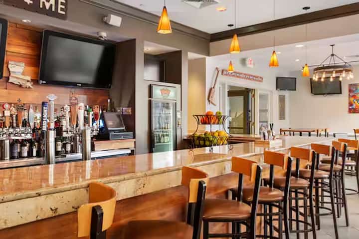 Casual sports bar dining area with orange seating, full bar counter, and pendant lighting