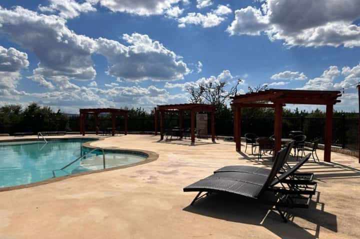 Outdoor pool deck with lounge chairs, red pergolas, and landscaped grounds under blue sky