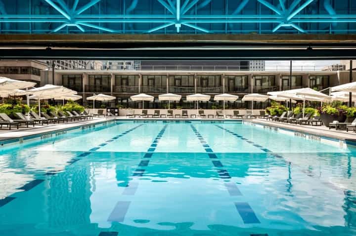 Olympic-sized lap pool with lane dividers, lounge chairs, white umbrellas, and modern building facade