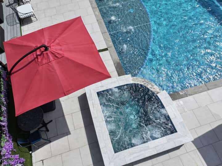 Red cantilever umbrella beside rectangular pool with white patio decking and spa jets