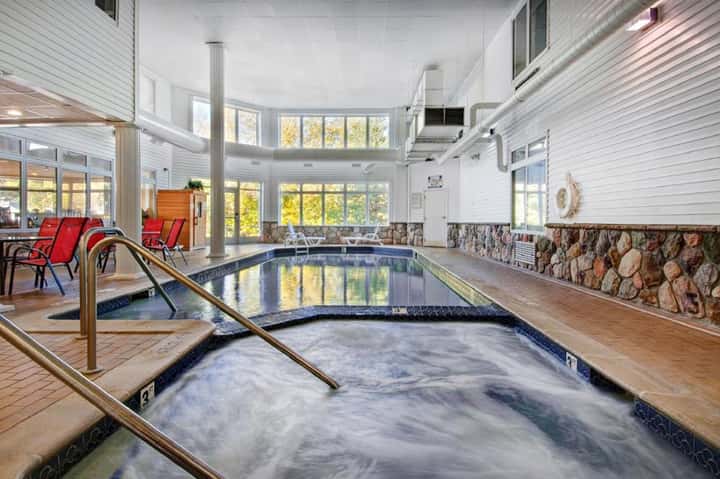 Indoor natatorium with lap pool and hot tub, stone accents, columns, and red lounge chairs