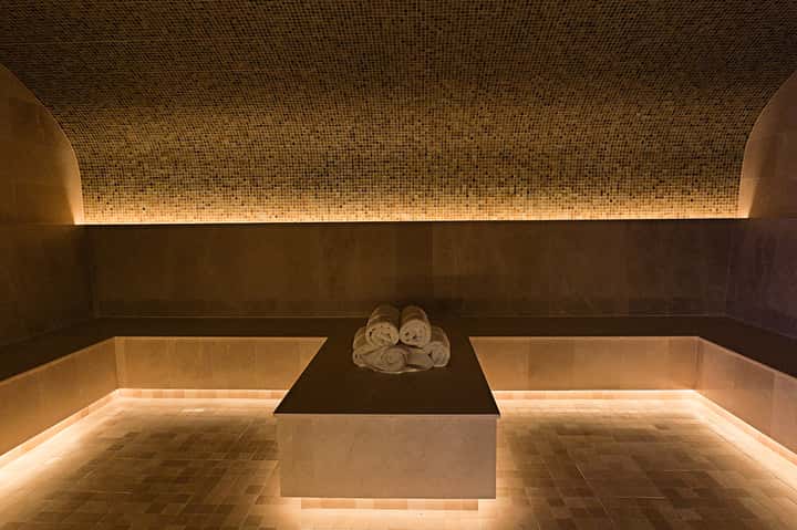 Luxurious spa treatment room with mosaic tile ceiling, heated stone basin, and rolled towels on dark stone platform