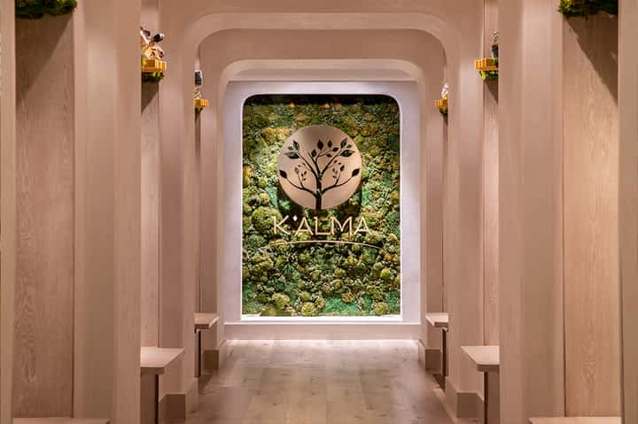 Modern spa entrance with moss wall and KALMA logo under rounded archway with wooden paneling