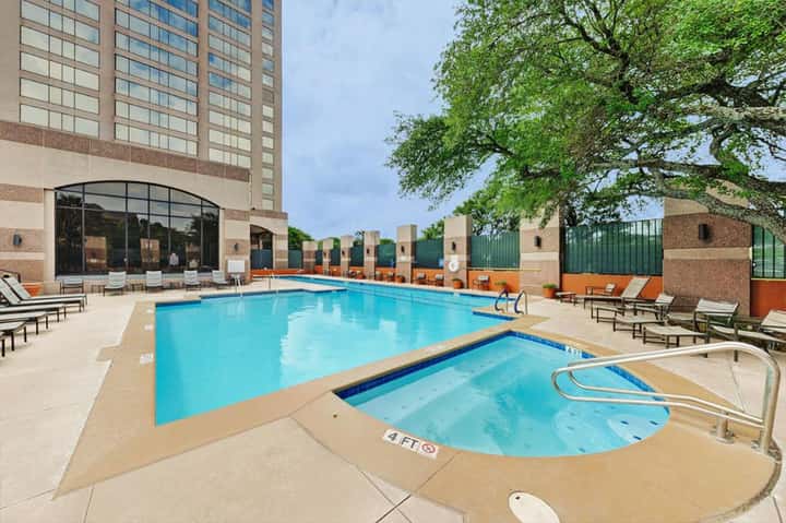 Urban hotel pool with blue water, lounge chairs, spa tub, and high-rise building backdrop