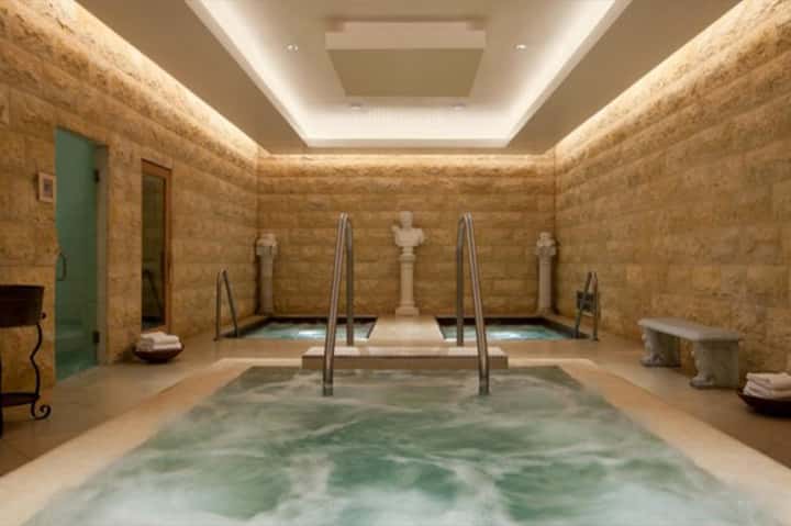 Spa bathhouse with warm stone pool, decorative Roman statues, natural light, and minimalist architecture