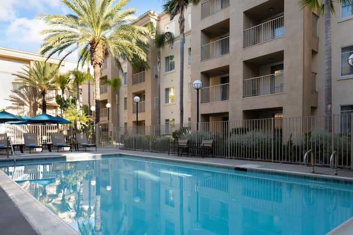 Resort pool with palm trees and lounge chairs in front of tan multi-story apartment building
