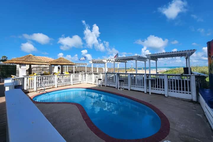 Small curved pool with white railings, tiki bar, and ocean horizon view