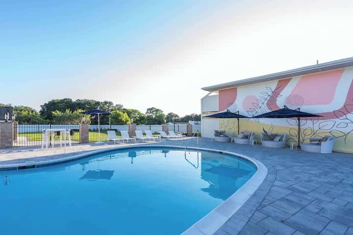 Curved resort pool with colorful mural wall art, lounge seating, umbrella, and surrounding landscape