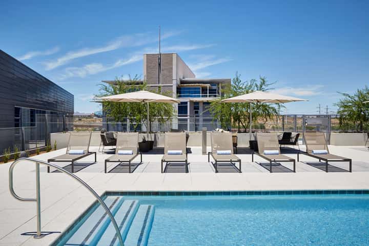 Modern rooftop pool area with white umbrellas, contemporary building, and desert landscape