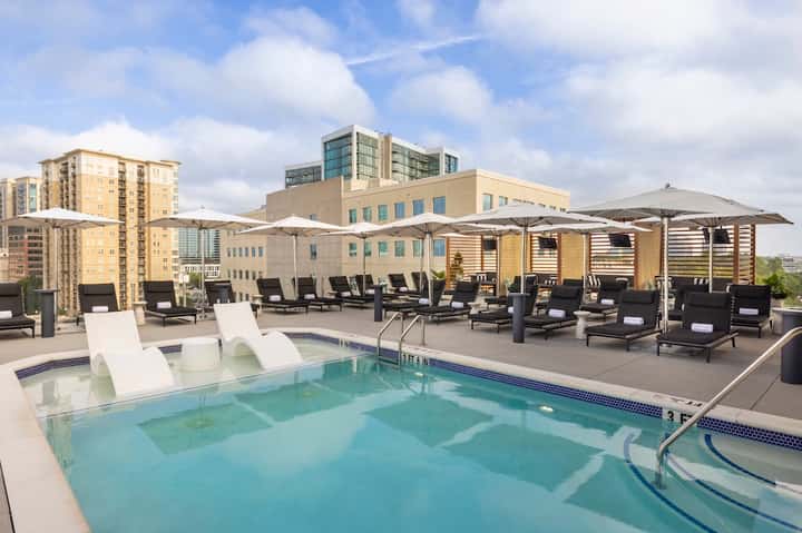 Rooftop pool deck with white umbrellas, lounge chairs, and city skyline backdrop