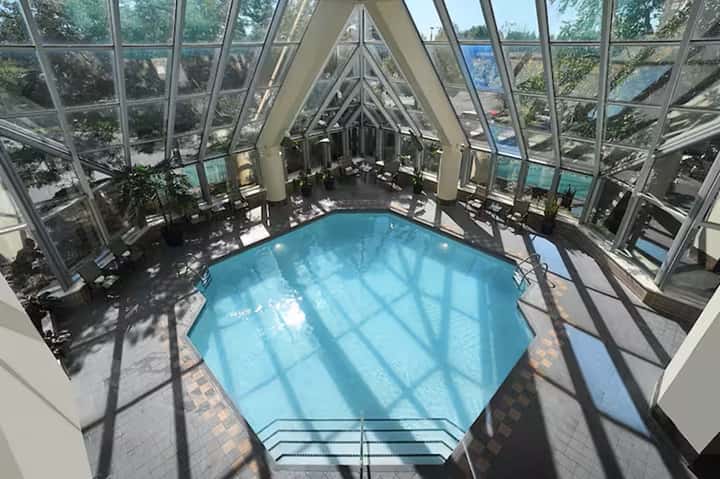 Glass-enclosed indoor pool with geometric ceiling beams and waterside seating