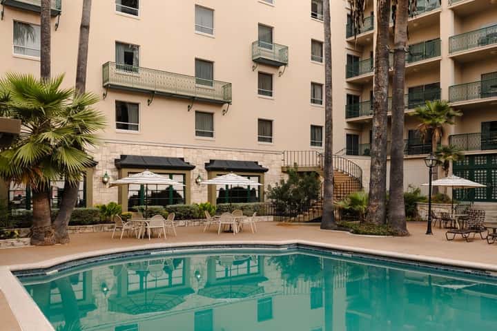 Hotel courtyard pool with multi-story building, palm trees, and dining area