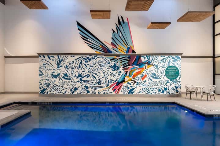 Indoor hotel pool with colorful bird mural and decorative wooden ceiling panels above