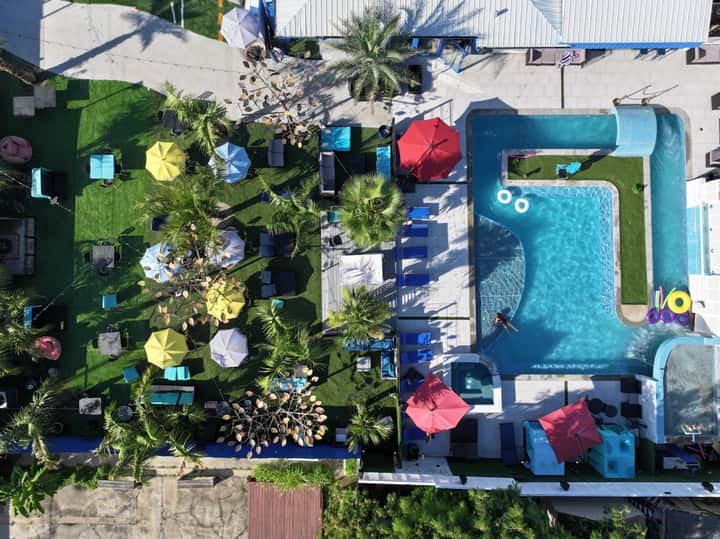 Aerial view of resort with turquoise pool, lush landscaping, colorful umbrellas, and lounge areas