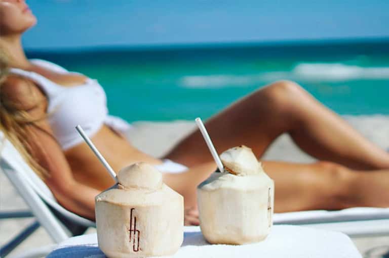 Woman relaxing on beach chair with coconut drinks and turquoise ocean view