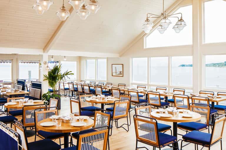 Bright dining room with wooden chairs, blue cushions, pendant lights, and expansive water views