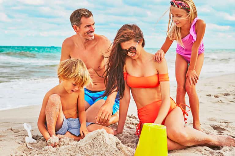 Family building sandcastle on beach with turquoise ocean and clear sky